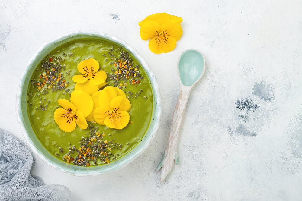 Zelená smoothie bowl ozdobená semínky a žlutými květy